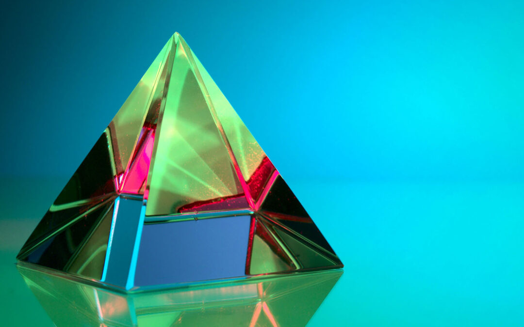 Pyramide aus Glas, von farbigem Licht durchdrungen, auf blauem Untergrund